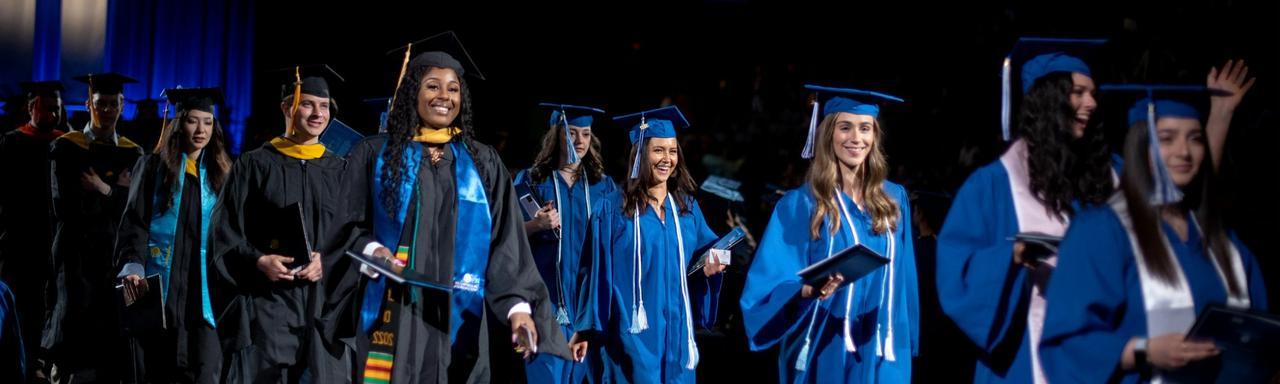 Graduates smile holding their diplomas at Commencement